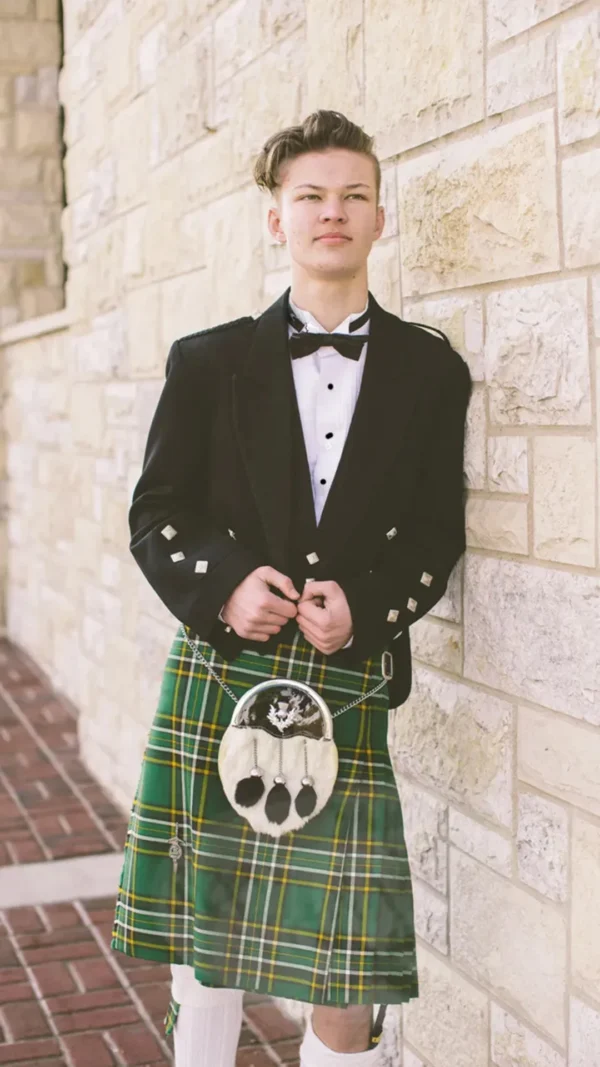 A man in a kilt and bow tie standing next to a wall.